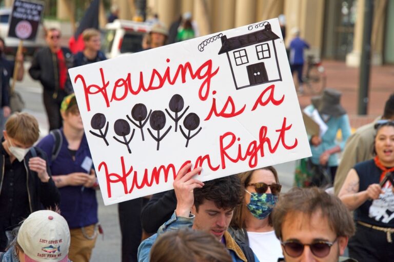 person in a protest carrying a poster saying "housing is a human right"