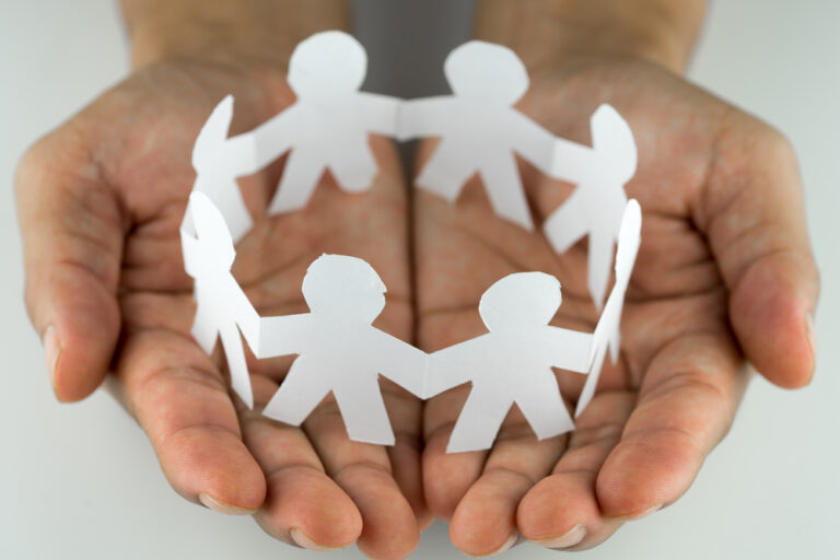 Hands carrying a paper circle made of stick figures holding hands